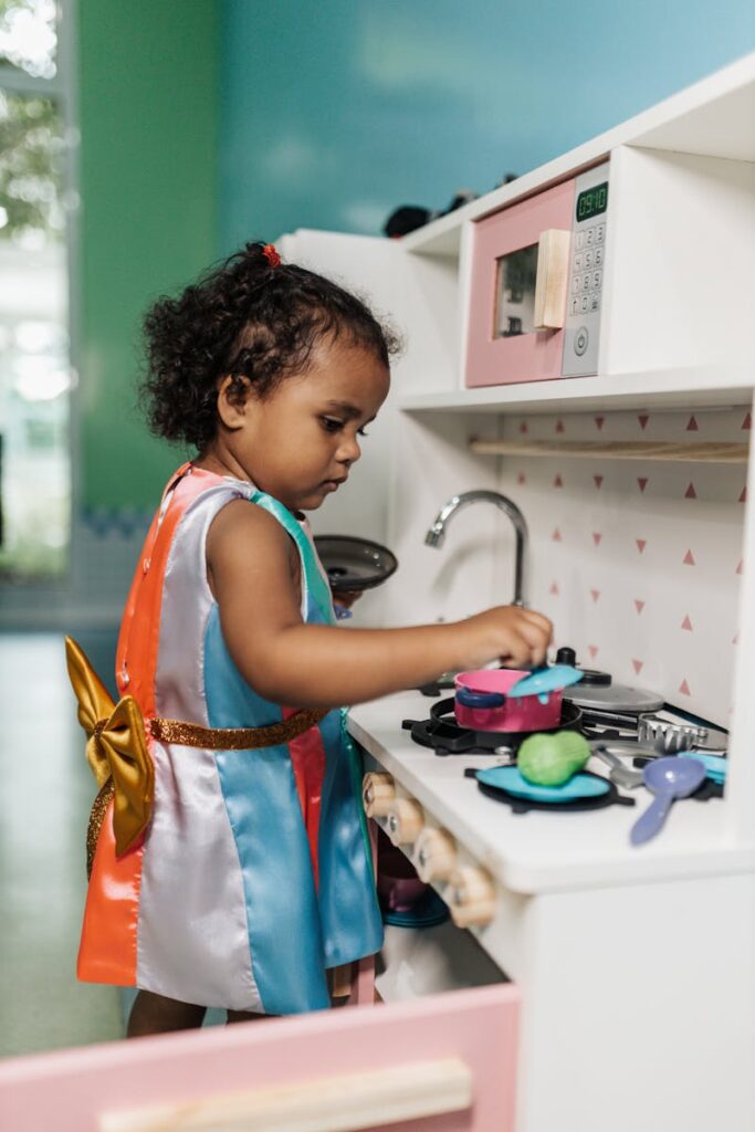 Photo by Matheus Bertelli Adorable child focused on pretend play in a toy kitchen indoors.