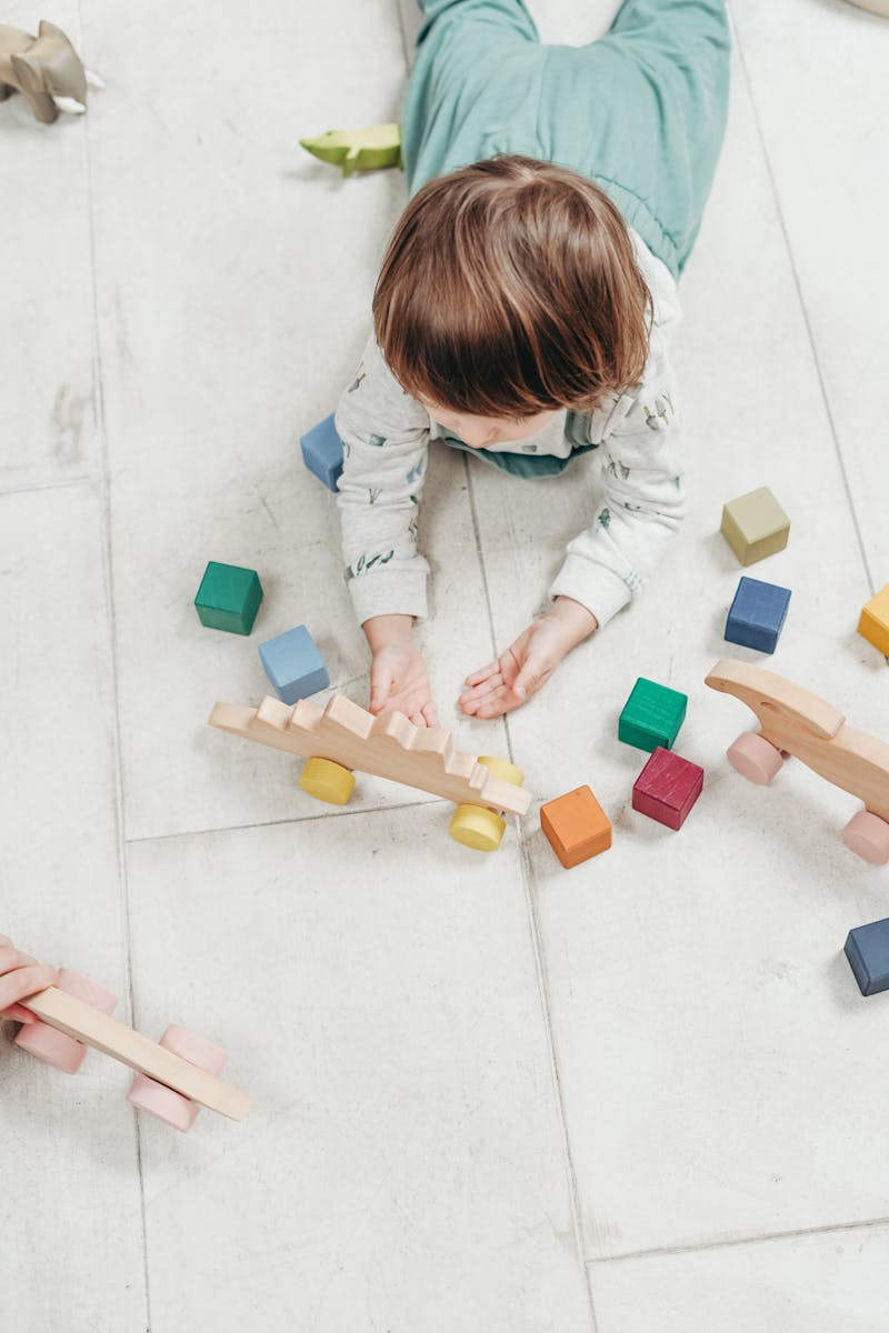 Settling in Child playing with colorful wooden toys on a light floor, creating a fun and educational setting.